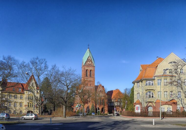 Kirche mit markantem Turm, umgeben von historischen Gebäuden, an einem sonnigen Tag.