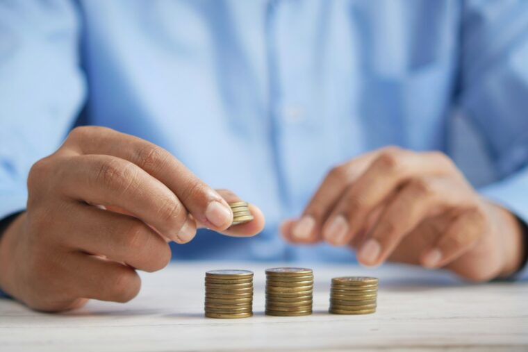 Ein Mensch in blauem Hemd stapelt Münzen auf einem weißen Tisch. Fokus auf Händen und Münzen.