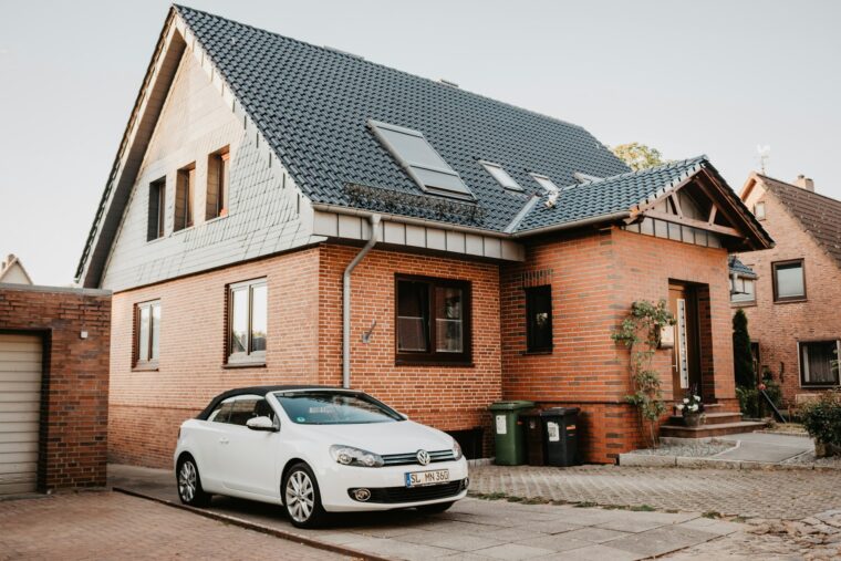 Ein modernes Backsteinhaus mit dunkelblauem Dach und weißen Fenstern. Ein weißer Volkswagen parkt davor.